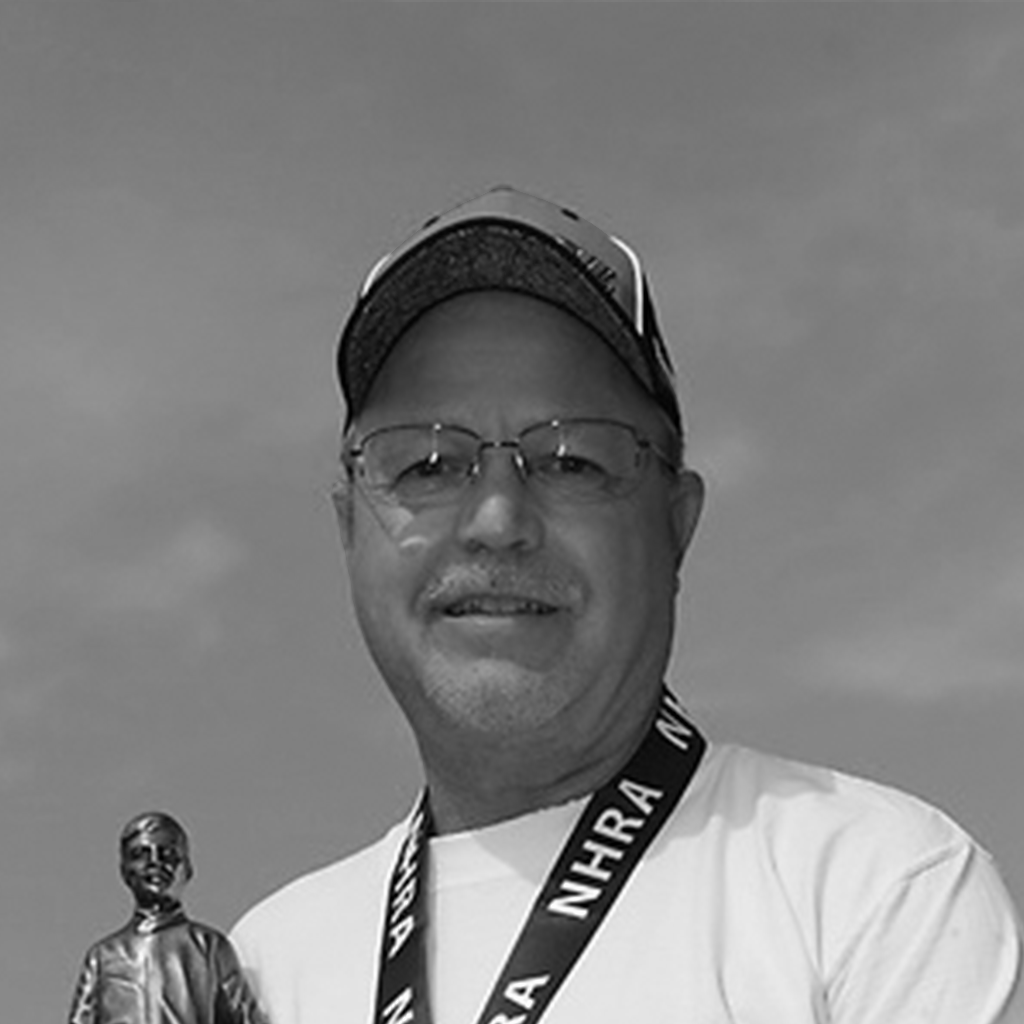 Gary Stinnett in black and white holding an NHRA trophy